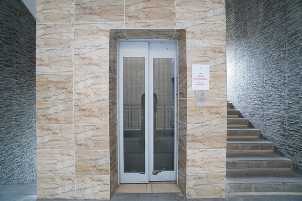 A building entrance with a stone facade and a glass elevator door. - Kamar Bagus (Jakarta)