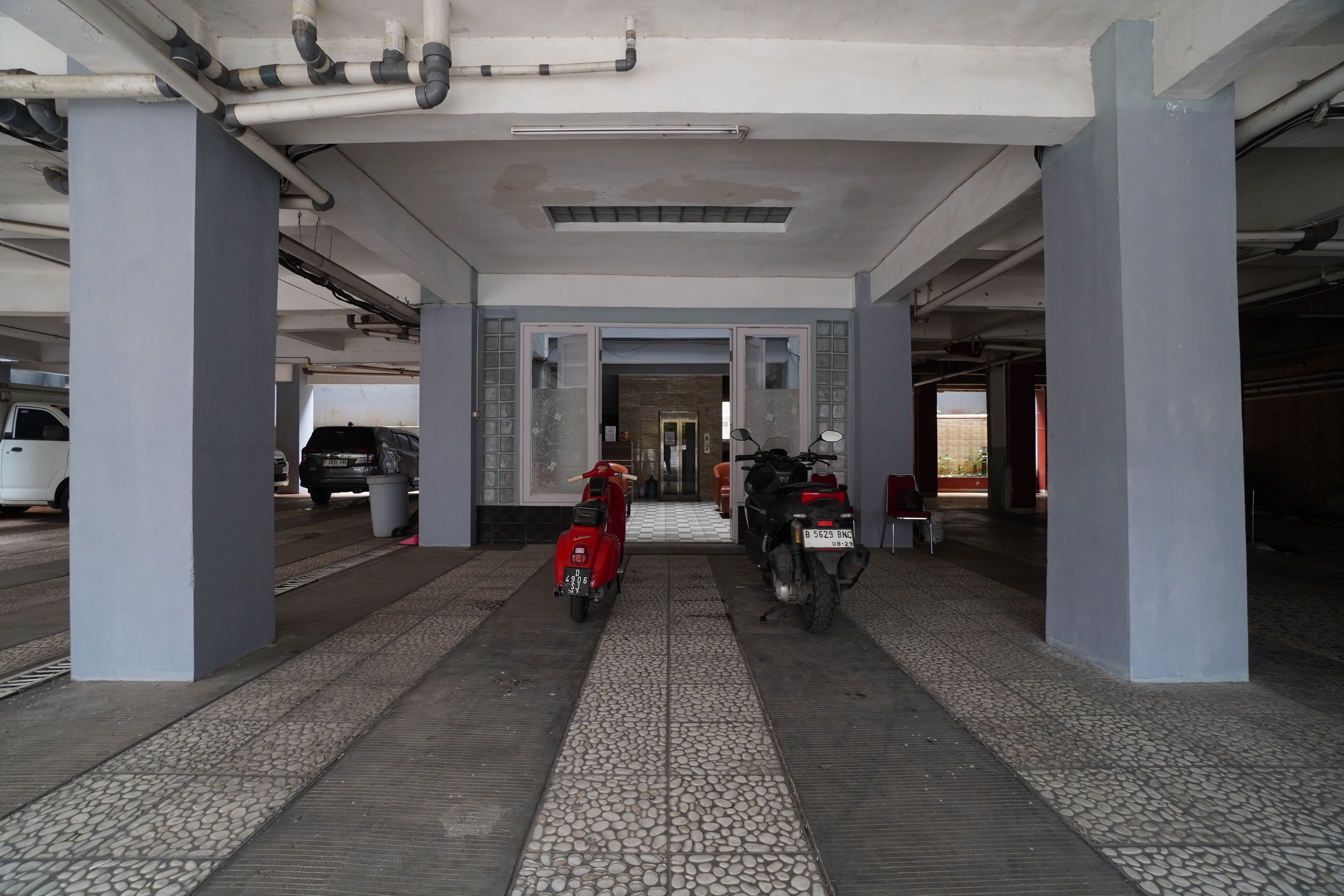 A covered parking area with tiled flooring, two scooters parked, and a white van in the background.