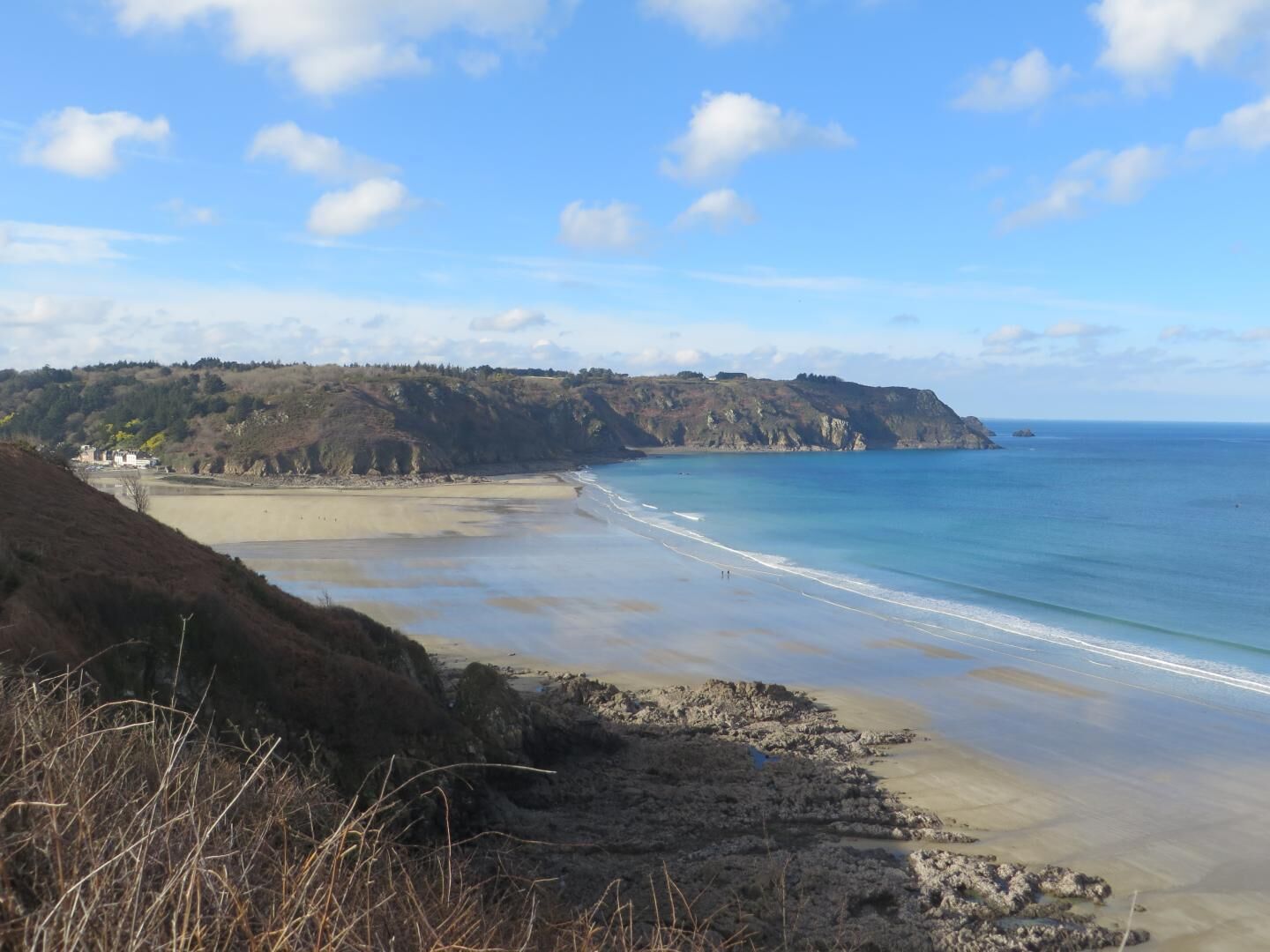 Un paysage côtier avec une plage, des falaises et un bâtiment visible au loin.