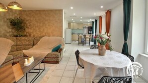 Ein modernes Wohnzimmer mit einer Couch, einem Couchtisch und einem Esstisch mit Stühlen. Im Hintergrund ist eine Küche zu sehen.