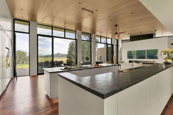 A modern kitchen with a large island, large windows, and a view of the outdoors.