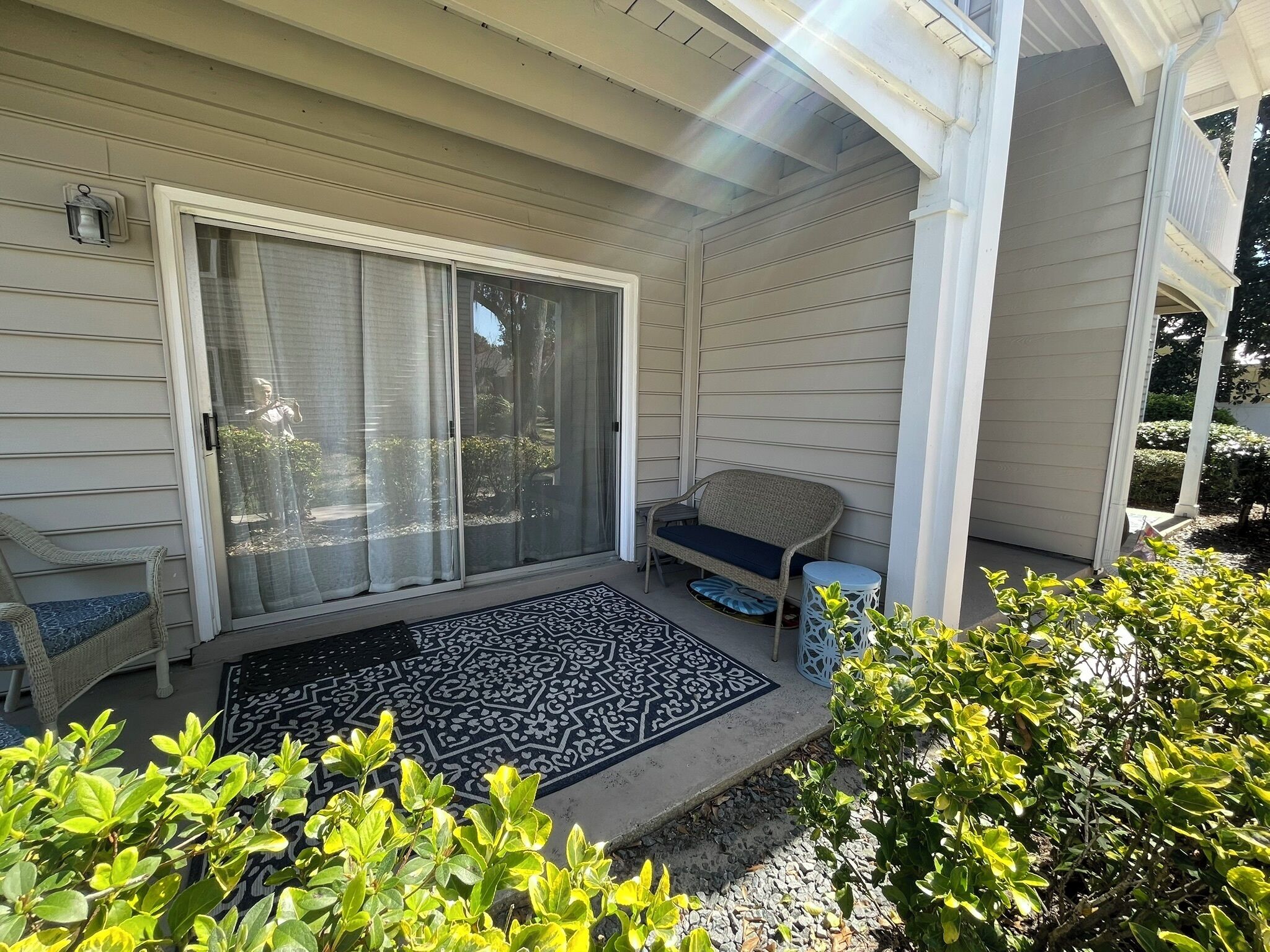 A covered porch with a sliding glass door, a wicker bench, a small round table, and a decorative rug.