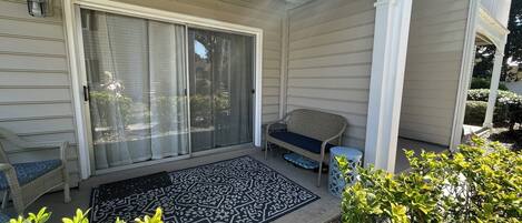 A covered porch with a sliding glass door, a wicker bench, a small round table, and a decorative rug.