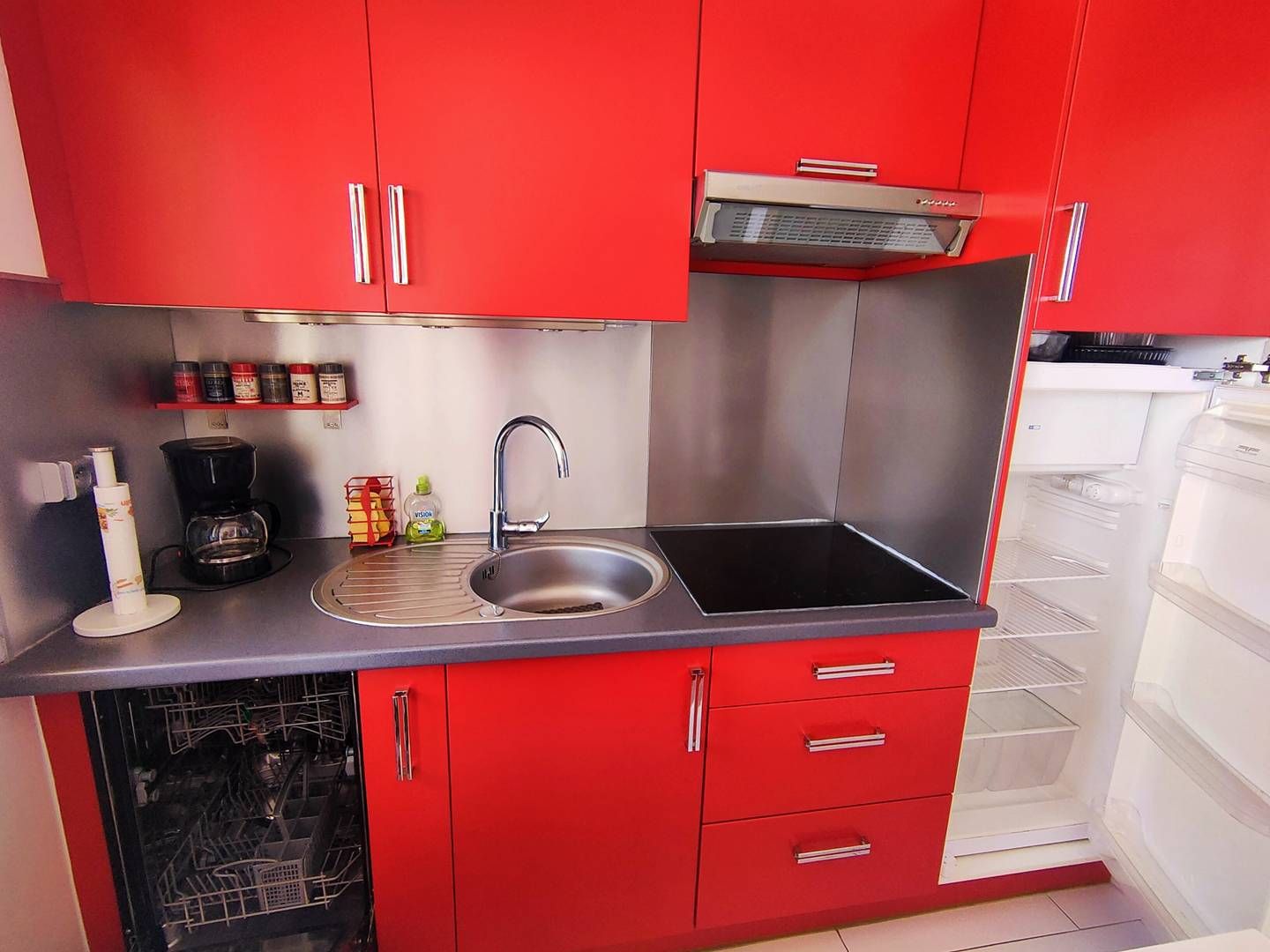 Une cuisine de taille réduite avec des meubles rouges, un évier en acier inoxydable et une machine à café.