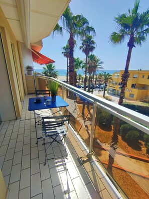 En balkon med bord og stole, der kigger ud over en strand og palmer.
