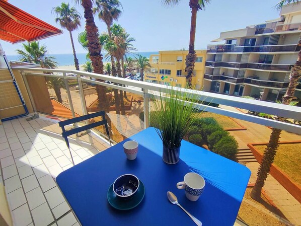 En balkon med et bord dækket til to, med udsigt over en strand og en bygning.
