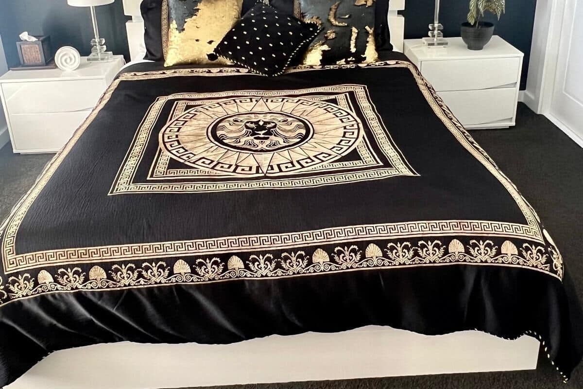 Un dormitorio con colcha negra y dorada, cabecera blanca y dos mesitas de noche con lámparas y adornos.