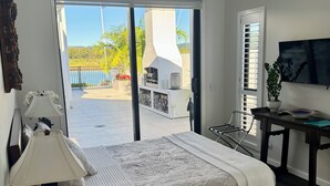 A hotel room with a bed, a desk, a TV, and a balcony with a view of the outdoors.