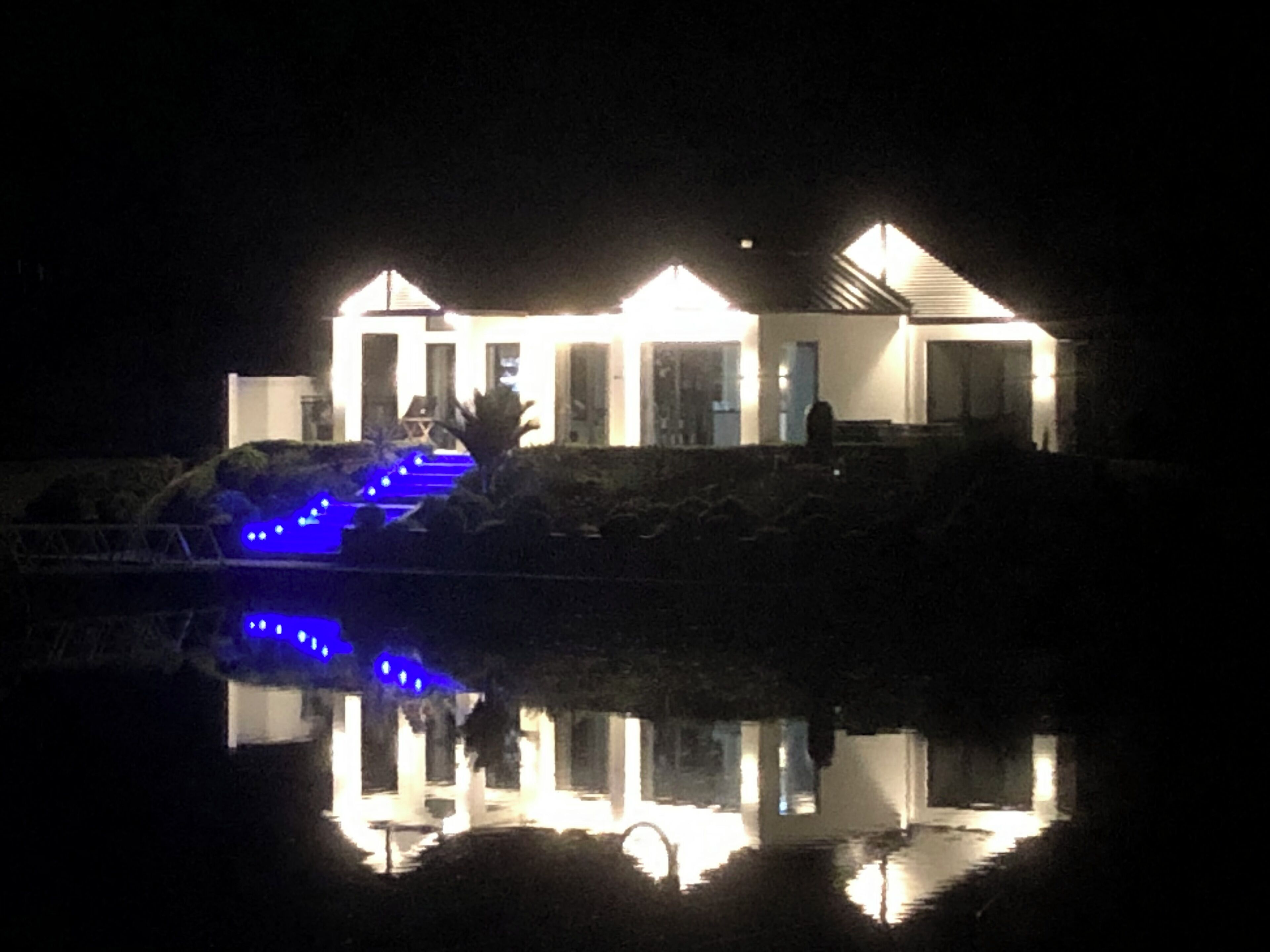 A house with a pool and blue lighting on the stairs.