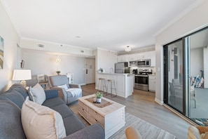 Una sala moderna con sofá, mesa de centro y área de cocina con refrigerador y microondas.