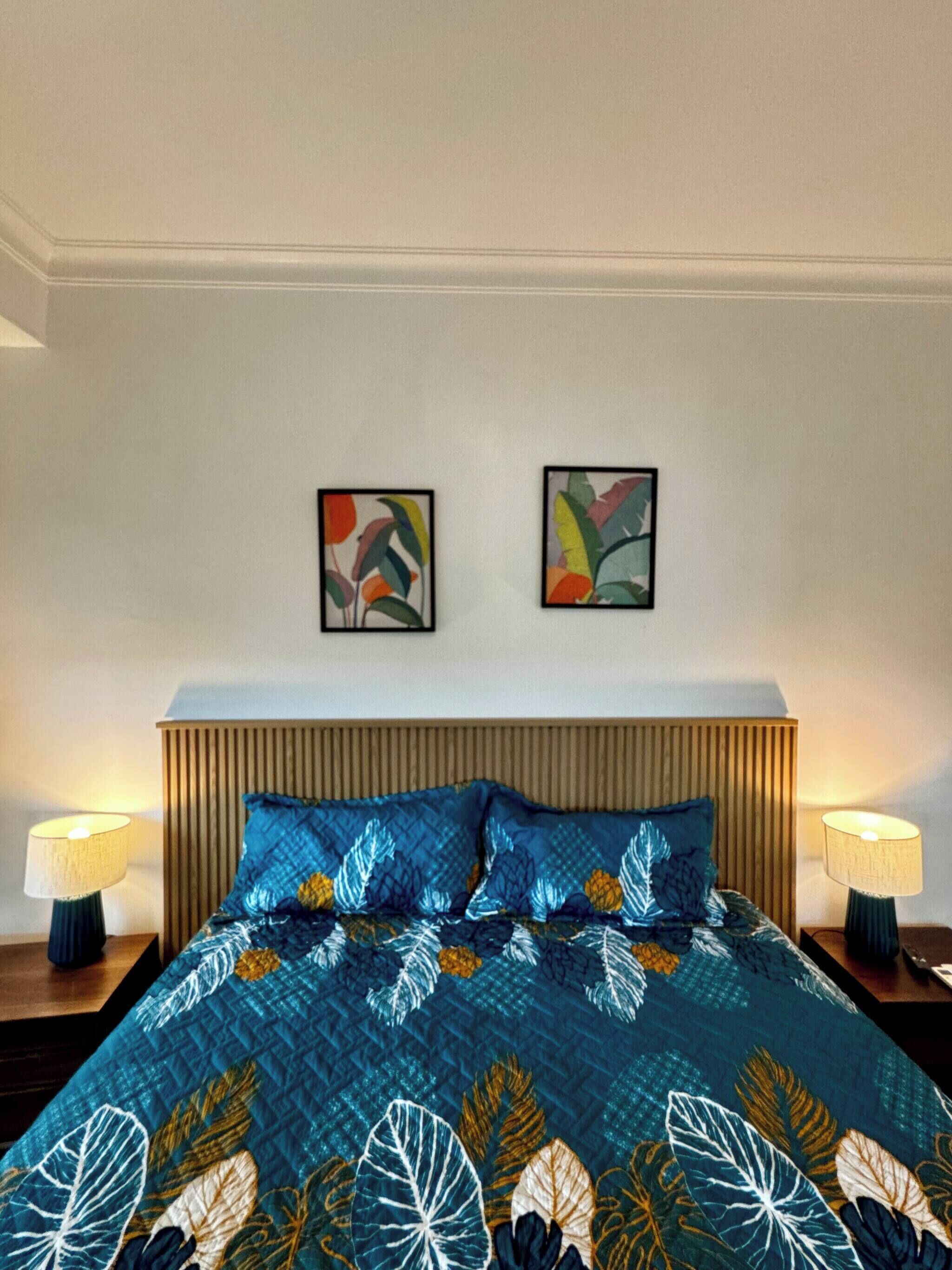 A bed with a blue floral bedspread, two wall-mounted paintings, and two bedside lamps.
