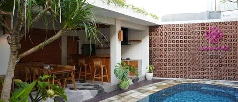 A modern outdoor pool area with a dining set and a kitchen adjacent to it.