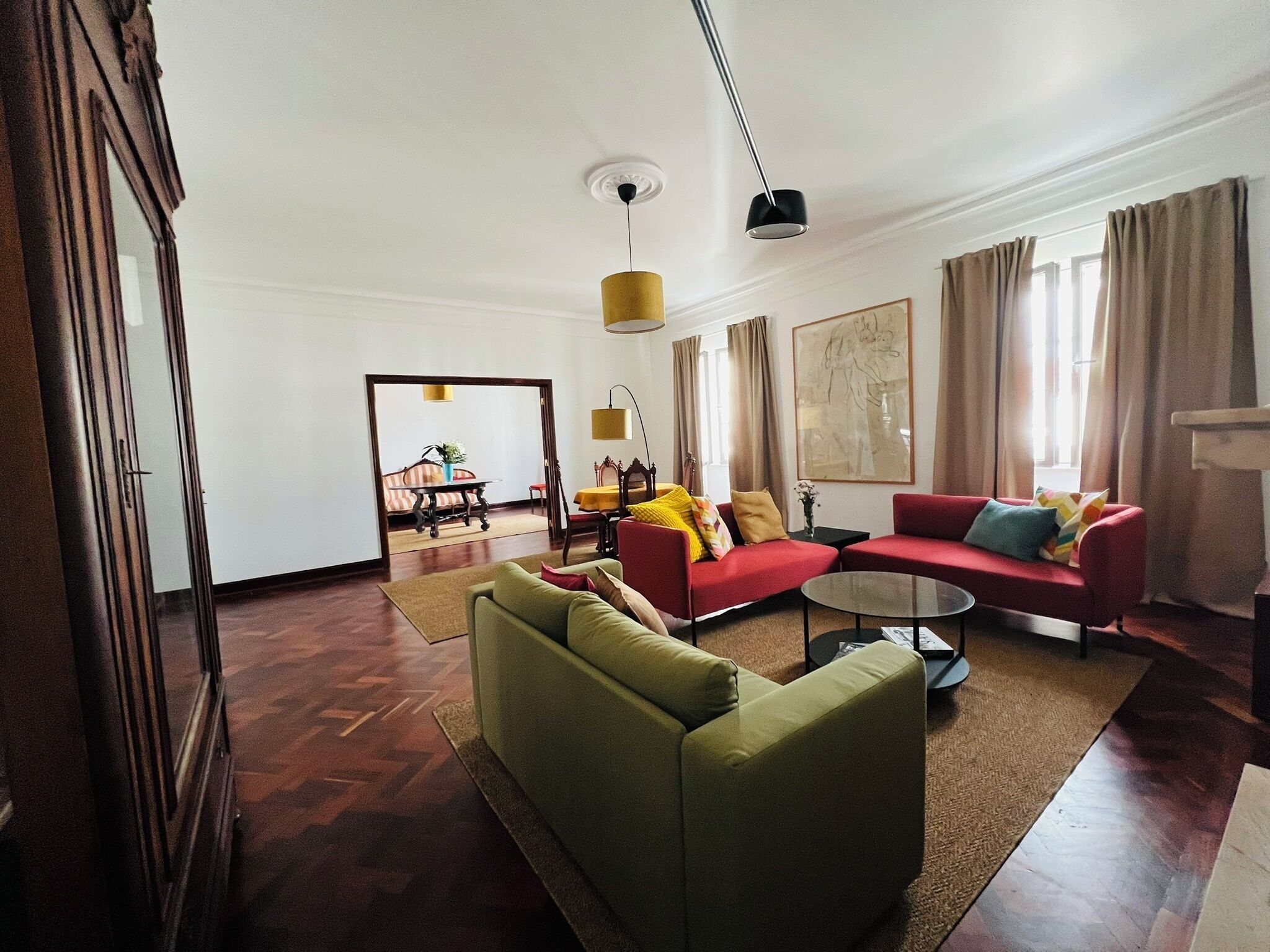 A spacious living room with a green sofa, a red sofa, and a small coffee table. There is a dining area with a table and chairs in the background.