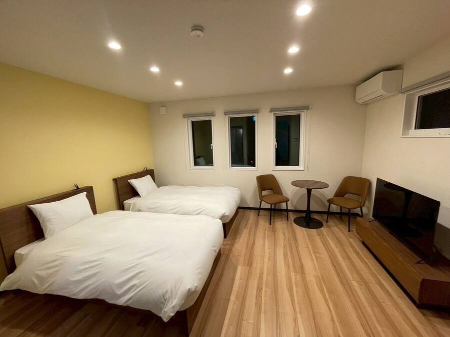 A hotel room with two beds, a TV, a small table, and two chairs.