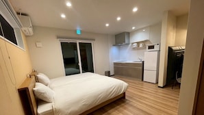 A compact hotel room with a bed, a kitchenette, and a sliding door leading to a balcony. - Casa Kokoro Hakuba (Hakuba)