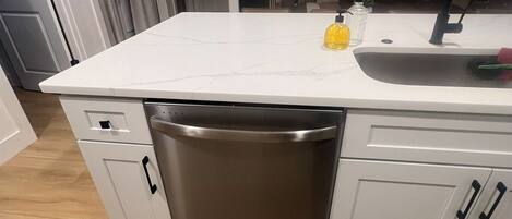 A modern kitchen with a white countertop, stainless steel dishwasher, and a sink.