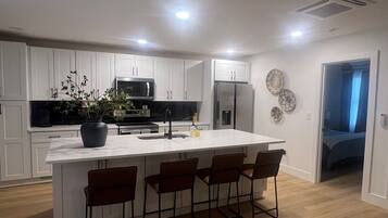 A modern kitchen with white cabinetry, a central island with bar stools, a microwave, refrigerator, and a sink.