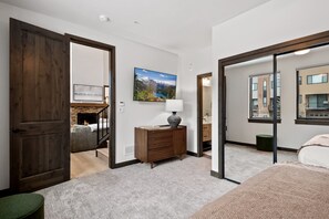 A bedroom with a large bed, a dresser, a painting, and a view of a building through a glass door. - Downtown WP Penthouse 221 I Private Hot Tub I Great Views I Triple Bunk I Discounted Attractions (Winter Park)