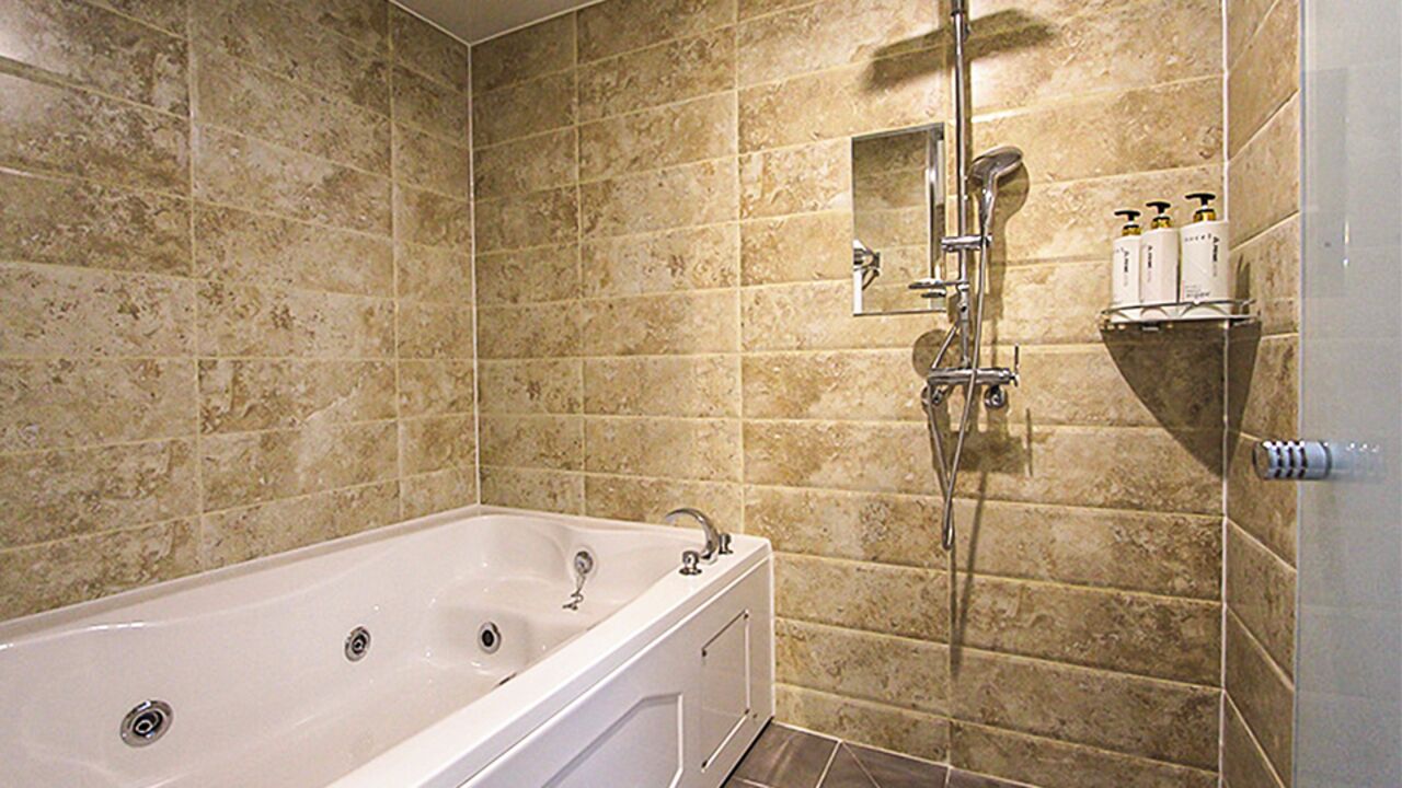 Une salle de bain équipée d’une baignoire, d’une douche et d’une étagère où sont rangés les articles de toilette.