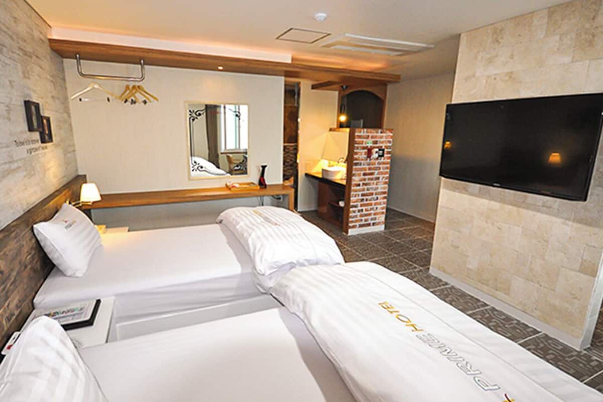 A hotel room with two beds, a TV, a mirror, and a brick wall.
