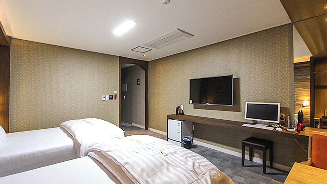 A hotel room with two beds, a desk with a computer, a TV, and a small refrigerator.