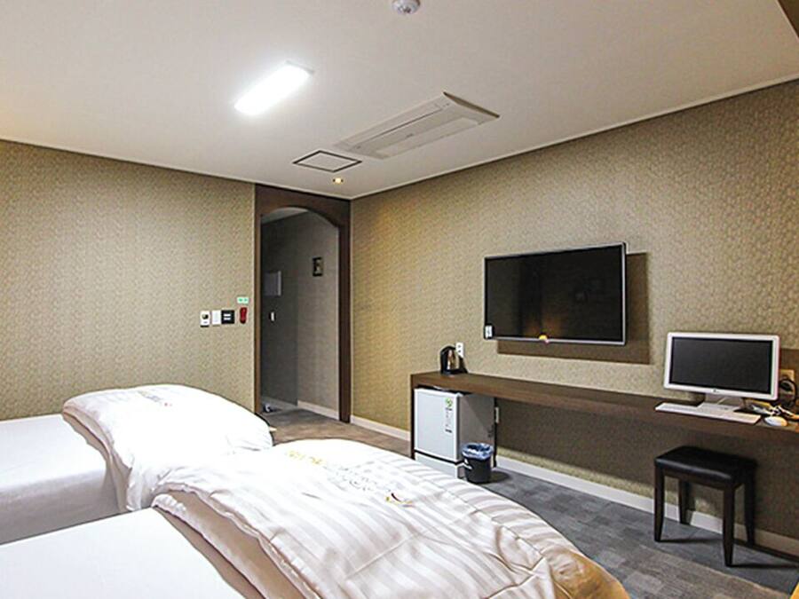 A hotel room with two beds, a desk with a computer, a TV, and a small refrigerator.