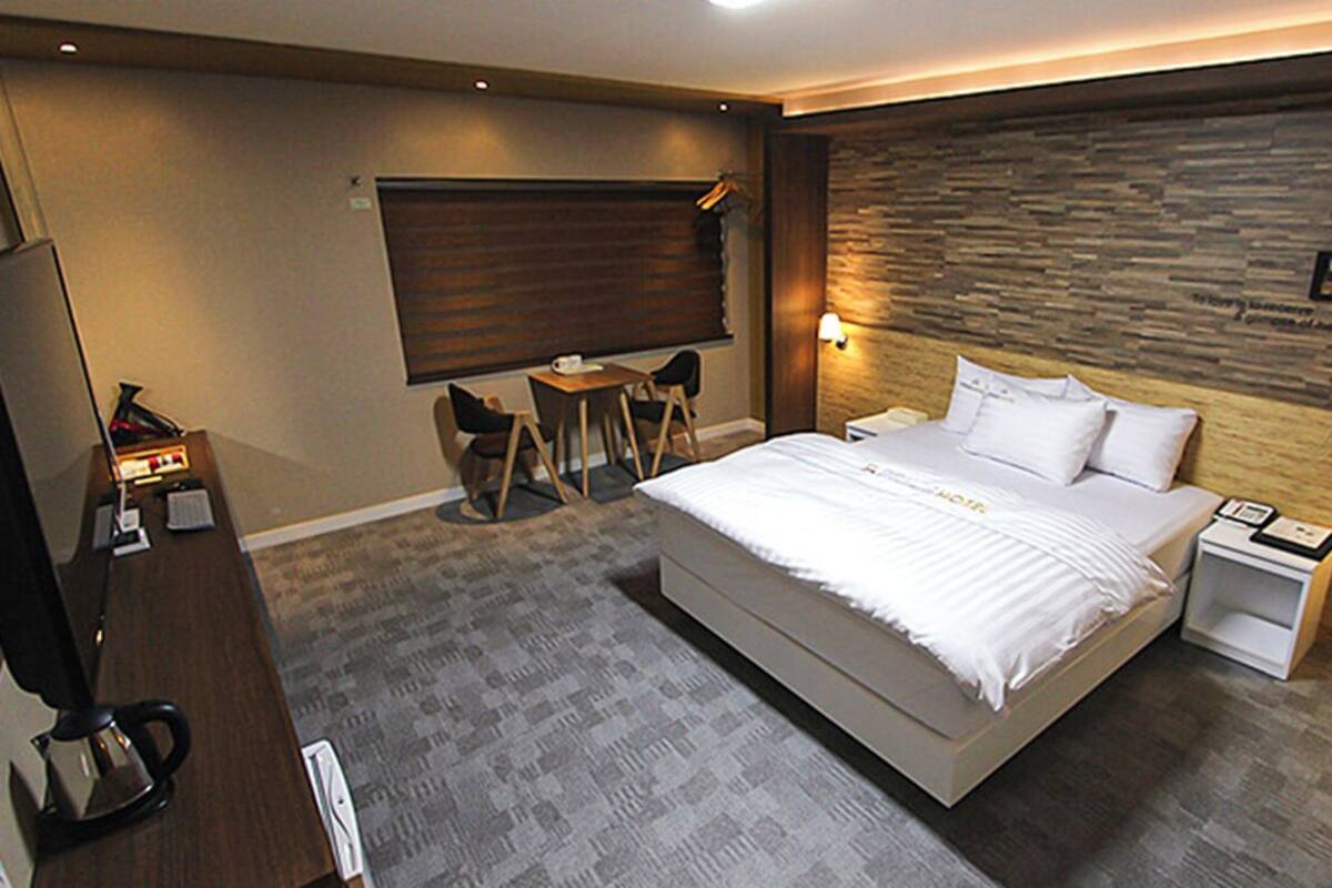 A modern hotel room with a large bed, a desk with a chair, a small table, and a TV.