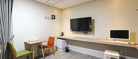 Een hotelkamer met een bureau, twee stoelen, een televisie, een computer en een klein krukje.