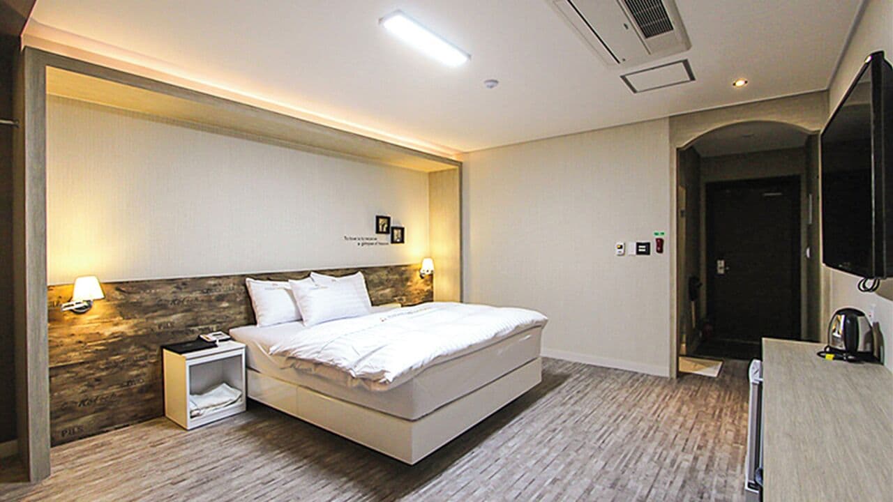 Une chambre d’hôtel moderne dotée d’un grand lit, de lampes de chevet, d’un mur décoratif en bois et d’un téléviseur à écran plat.