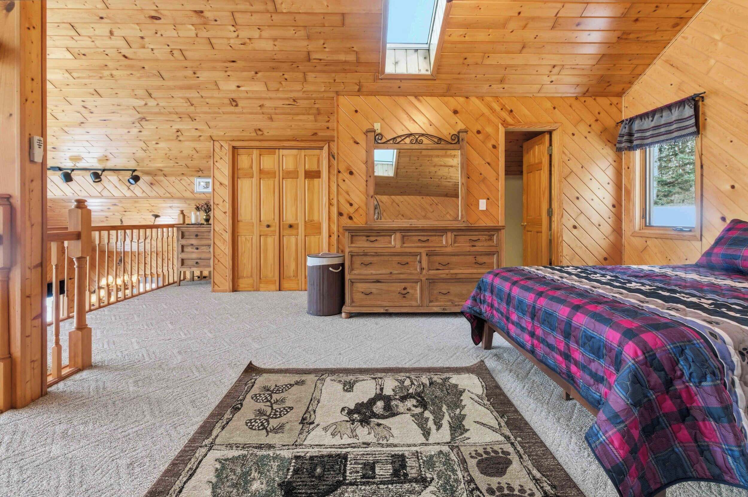 Een houten slaapkamer met een bed, een dressoir en een grote spiegel.