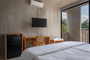 Et moderne hotelværelse med en seng, et skrivebord, en stol, et fladskærms-tv og et lille, sort køleskab.
