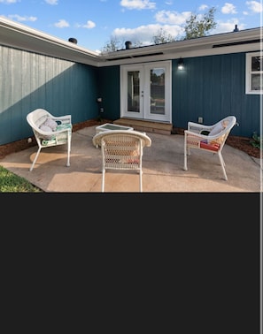 A patio with three wicker chairs and a small table, a sliding glass door, and a blue exterior wall.