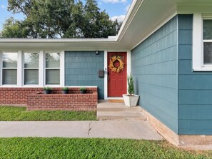 A house with a red door, a wreath, and a brick foundation.