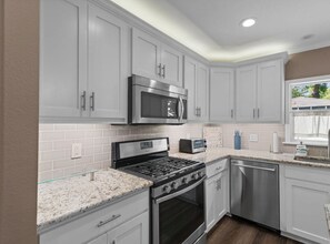 A modern kitchen with white cabinets, stainless steel appliances, and a granite countertop.