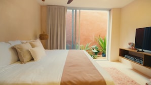 A bedroom with a large bed, a television, a coffee maker, and a view of a garden through a sliding door. - El Iguano, beautiful room with interior Garden (Mérida)