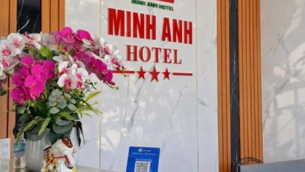 A reception desk with a sign for Minh Anh Hotel, a vase of flowers, and a QR code. - Minh Anh Hotel (Hung Nguyen)