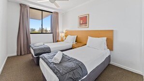 Habitación de hotel con dos camas, un ventilador de techo, una ventana con cortinas y un cuadro en la pared.