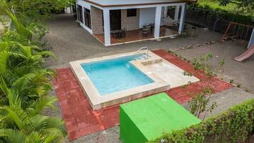 Piscina retangular com pequena área de deck, ladeada por um deck revestido com azulejos vermelhos e verdes.