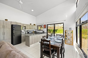 Una cocina moderna con una isla central, comedor con mesa de vidrio y amplios ventanales que ofrecen vistas al exterior.