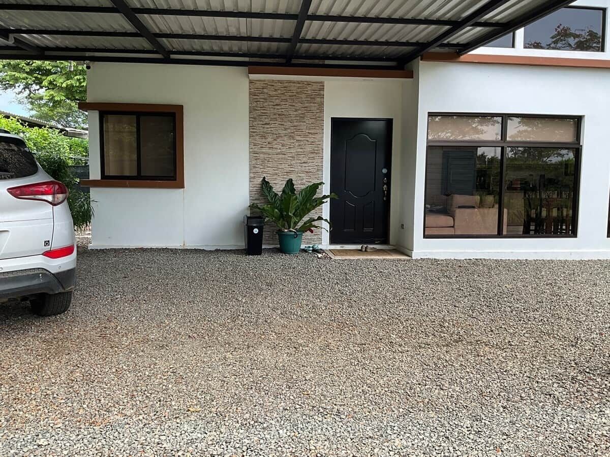 A modern house with a gravel driveway, a white car parked on the left, and a black door with a small window.