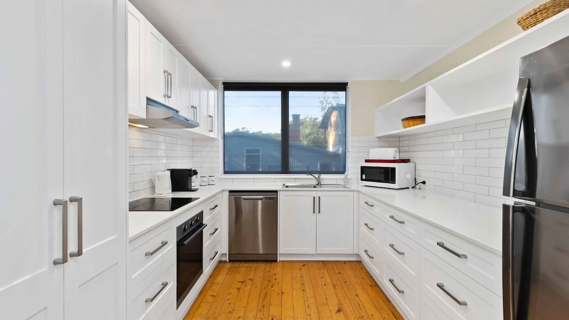 A modern kitchen with white cabinetry, stainless steel appliances, and a wooden floor.