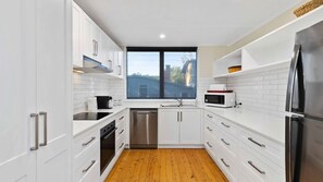 A modern kitchen with white cabinetry, stainless steel appliances, and a wooden floor. - Bendalong Beachside near Washerwomans Beach (Bendalong)