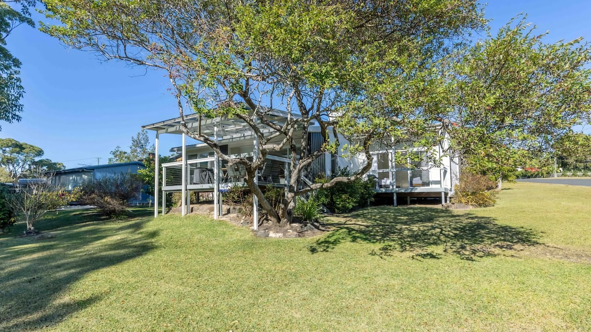 Une maison dotée d’un espace extérieur abrité, entourée d’une pelouse bien entretenue et d’arbres.