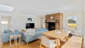 A modern living room with a fireplace, a flat-screen TV, a dining area with a wooden table and chairs, and a sofa set. - Bendalong Beachside near Washerwomans Beach (Bendalong)