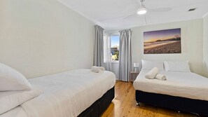 A hotel room with two beds, a ceiling fan, a window with curtains, and a painting on the wall. - Bendalong Beachside near Washerwomans Beach (Bendalong)