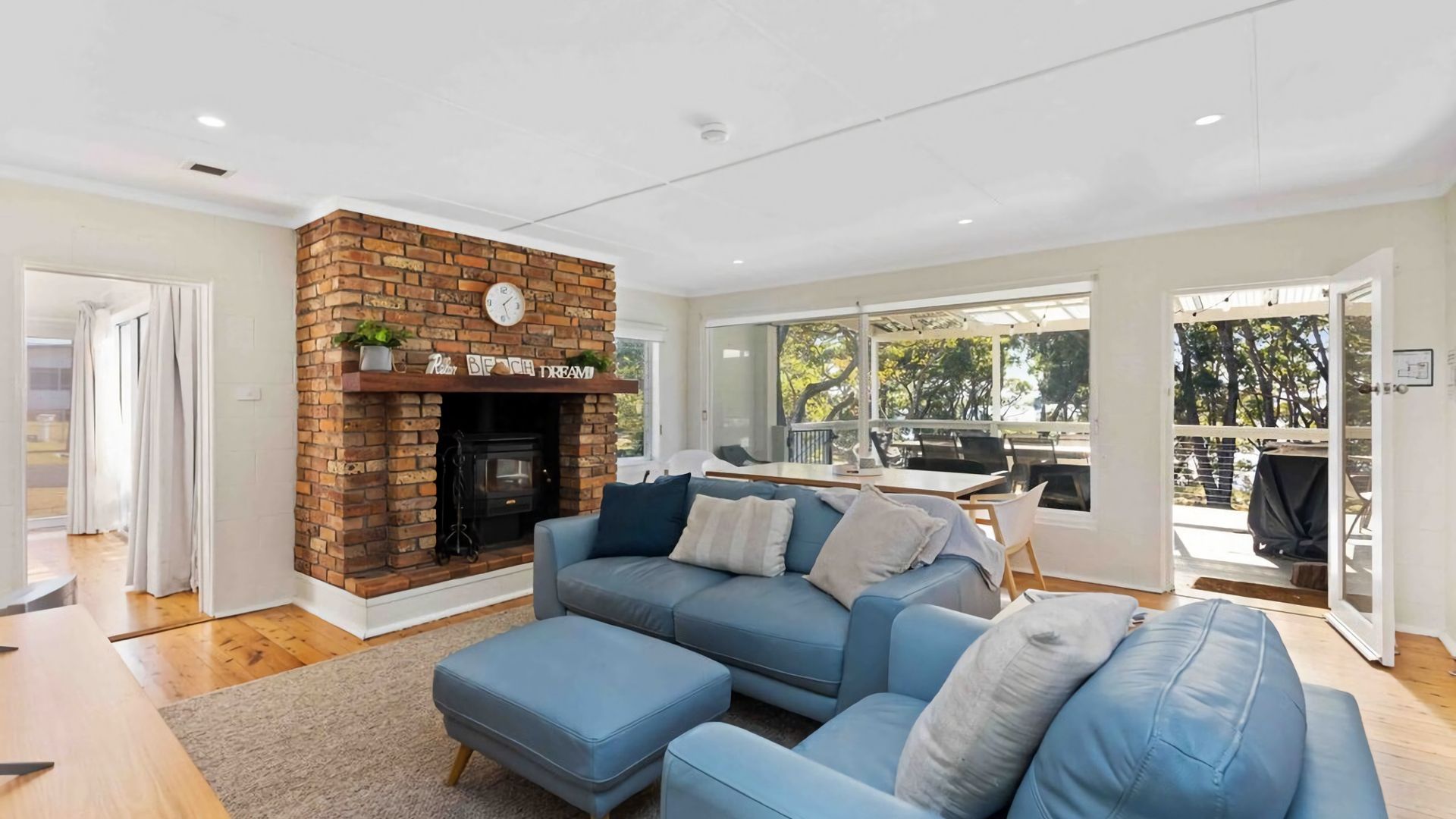 A living room with a brick fireplace, a blue sofa set, and a dining area with outdoor seating.