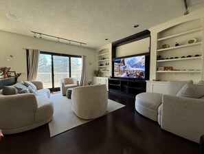 A modern living room with a large flat-screen TV, two sofas, a coffee table, and a bookshelf. - Luxury Executive Home 6000 sq ft 5 bedrm central location with AC and fitness rm (Calgary)