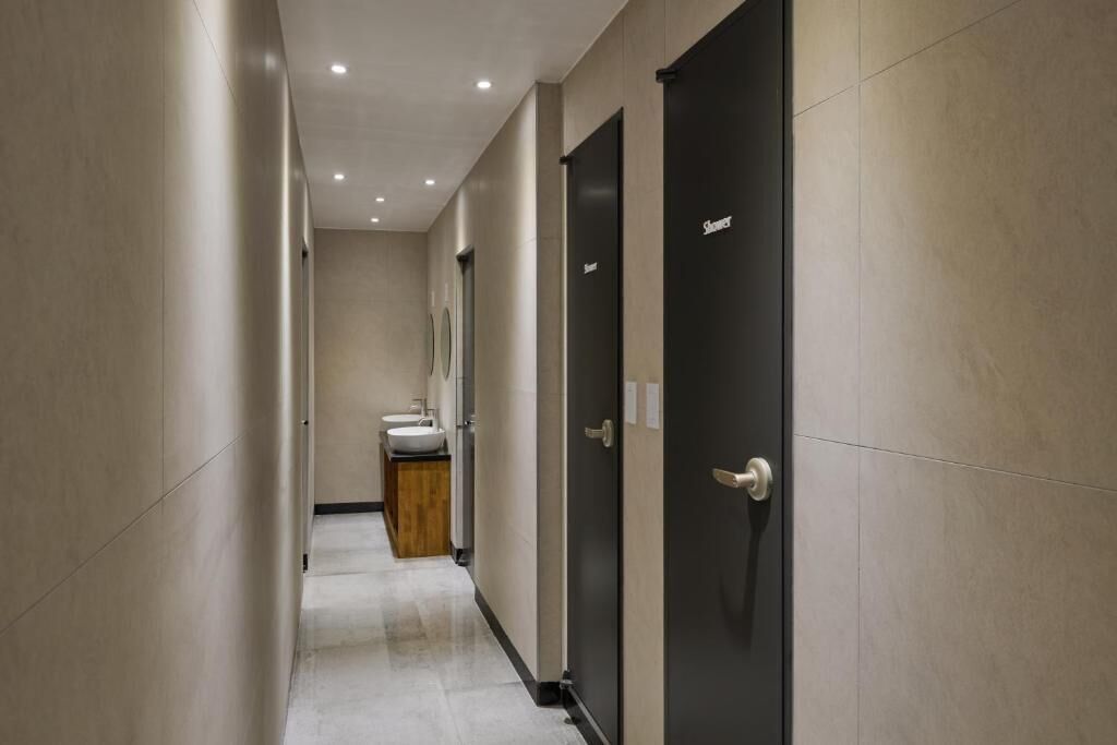 Un couloir moderne et bien éclairé, avec un lavabo et un miroir au bout, qui mène à une porte sombre dotée d’une poignée.