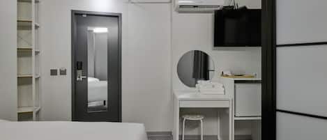 A modern hotel room with a bed, a desk with a chair, a mirror, a wardrobe, and an air conditioning unit.