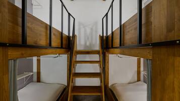 Dormitorio con literas, una escalera central, paredes de madera y ropa de cama blanca.